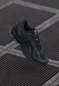 Baskets de running noires avec upper en mesh, détails texturés et système de laçage. Présente un logo notable et une semelle rembourrée pour le confort.