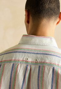 Ribašärk, millel on pastelsetes toonides nagu sinine, roheline, roosa ja valge. Valmistatud pehmest kangast, millel on nööpidega krae ja ventilaatorite detailid.