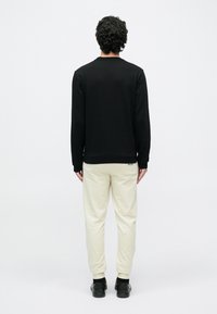 Μαύρο πουκάμισο μακρυμάνικο με στρογγυλή λαιμόκοψη, συνδυασμένο με ανοιχτό μπεζ στενά στενόμενα παντελόνια jogging, και τα δύο με ομαλή υφή και μινιμαλιστικό σχέδιο.