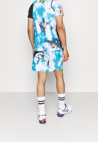 Modrý a bílý tie-dye sportovní set, krátký rukáv a odpovídající šortky, s černými akcenty a detaily loga. Bílé ponožky s černými pruhy.
