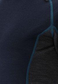 Mörkblå och mörkgrå textil med en mjuk yta, med kontrasterande sömmar i turkos och en figurnära design.