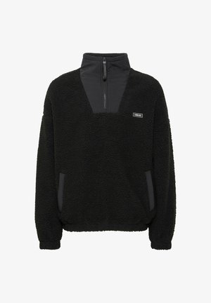 Mustpea fliispullover kõrge krae ja lukuga, kontrastsed siledad paneelid. Omab küljetaskuid ja tekstureeritud pinda.