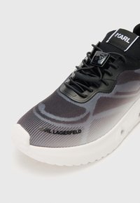 Svart og grå sneaker med gradientmønster, pustende tekstiloverdel, sikker lissesystem og hvit gummisåle med logodetalj.