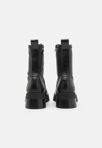 Stivali neri in pelle alla caviglia con una finitura lucida, dotati di chiusura con zip e tacco spesso e chunky. Texture liscia e dettagli cuciti.