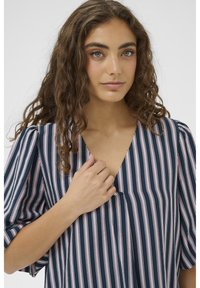 Bluza cu dungi bleumarin și roz, cu decolteu în V, mâneci scurte bufante și textură moale și fină. Prezintă linii verticale pentru un aspect alungit.