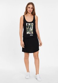 Melna tanks top ar krāsainu grafisko apdruku ar uzrakstu "ENDLESS SUMMER" un melnu svārku. Apģērbu papildina baltas sporta kurpes.