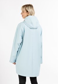 Giacca impermeabile azzurro chiaro con cappuccio, caratterizzata da una vestibilità ampia, maniche lunghe e dettagli con bottoni a pressione. Texture liscia e lucida.