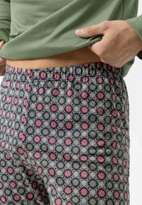 Pyjamabroek in gemusterde stof met rode bloemen, groene cirkels en een zwarte achtergrond. Elastische tailleband voor comfort.