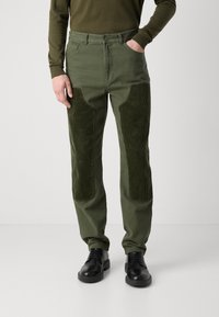 Olive green pants made of cotton with corduroy knee patches. Features a straight leg design and classic button closure. Worn with black shoes.