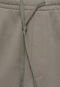 Un pantalon de survêtement gris clair avec une surface texturée, une taille élastique et un cordon de serrage de couleur assortie pour l'ajustement.