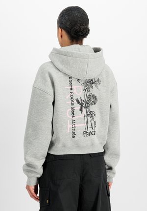 Person, die von hinten gesehen wird, trägt einen hellgrauen Hoodie mit floraler Skizze und den Worten ‚Roots‘ und ‚Peace‘ in Kombination mit schwarzen Cargo-Hosen.