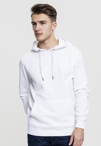 Sudadera blanca con bolsillo frontal, capucha con cordón y puños de canalé. Textura de tela suave, diseño minimalista, adecuada para el uso casual.