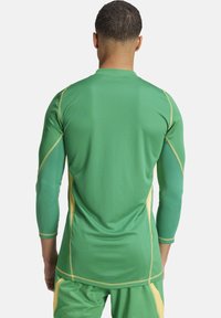 Groen sportief longsleeve shirt met gele accenten, geribbeld textuur en een getailleerd ontwerp. Beschikt over vlakke naden en een neklijn met een hoge kraag.