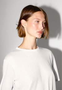 Witte katoenen t-shirt met een ronde halslijn, voorzien van korte mouwen en een relaxte pasvorm, getoond tegen een neutrale achtergrond met zachte verlichting.
