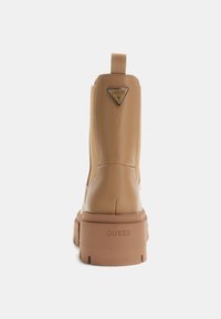 Stivaletti alla caviglia in ecopelle beige con suola robusta e strutturata, linguetta sul retro e logo triangolare a marchio accentuato sul tallone.
