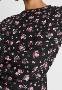 Černá blůza s dlouhými rukávy, s květinovým vzorem v růžové a zelené barvě. Látka má hladkou strukturu s mírným nařasením.