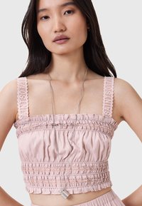 Lyserød cropped top med blondebesatte stropper, smocket tekstur og volangkant. Modellen bærer en sølvvedhængs halskæde.