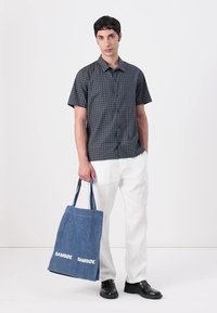 Korte ermer marineblå skjorte med geometrisk mønster, hvite lette bukser og en blå totebag med "SAMSOE" i hvit tekst.