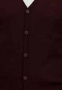 Donker burgundy knoop cardigan met vier knopen over een wit patroonshirt, met een klein geborduurd logo bij de schouder.