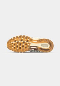 Semelle de chaussure de course en caoutchouc marron et beige avec des motifs de semelle circulaires et rectangulaires. Présente un intercalaire blanc et un détail d'unité d'air.