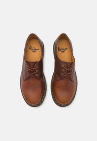 Braune Leder-Doktor Martens Schuhe mit einer glatten Oberfläche, runder Zehenpartie und kontrastierenden gelben Nähten entlang der Sohle. Flache Schnürsenkel und minimalistische Details.