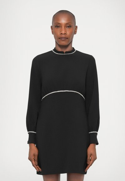 Robe noire à manches longues et col haut, avec une taille cintrée et des embellissements argentés le long de l'encolure et de la taille.