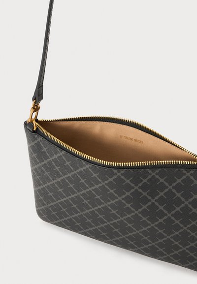 Pochette à motif noir avec fermeture éclair dorée partiellement ouverte, révélant un intérieur en tissu beige et une quincaillerie dorée fixant la sangle.
