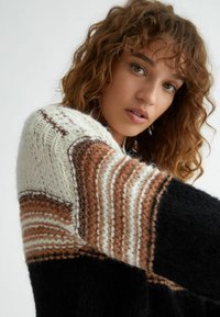 Maglione lavorato a maglia multicolore con strisce marroni, crema e nere. Motivo testurizzato con spessori e morbidezze variabili.