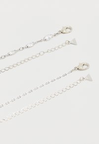 Deux rallonges de chaîne en argent avec fermoirs homard ; une chaîne présente des pierres ovales transparentes, l'autre des maillons ronds simples, chacune avec une étiquette triangulaire à l'extrémité.