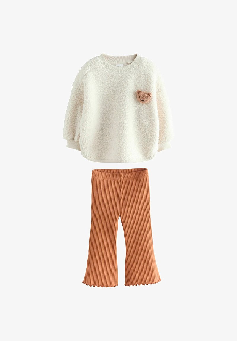 Cream-colored textured long-sleeve top with teddy bear patch paired with ribbed, flared rust-orange pants for children.
