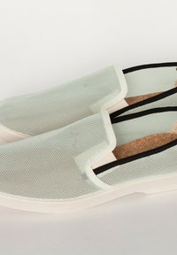 Baskets à enfiler en maille vert clair avec des accents noirs, dotées d'une semelle en liège et d'une semelle en caoutchouc blanche. Texture lisse et design minimaliste.
