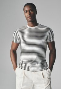 Stribet sort-hvid kortærmet t-shirt i blødt stof med rund halsudskæring, parret med lyse skræddersyede bukser.