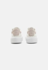 Sneaker mit einem weißen Lederoberteil, pinkem Wildleder-Ferseneinsatz und weißer Gummisohle mit gerippter Textur. Minimalistisches Design und keine sichtbaren Marken.