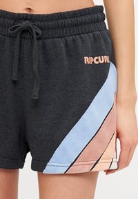 Pantalones cortos de color gris oscuro con cinturilla elástica y cordón. Presenta rayas diagonales en azul claro y melocotón, con un logo "Ripcurl" en rosa.