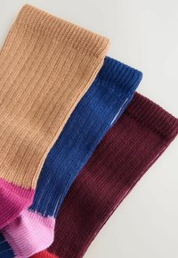 Three pairs of socks in tan, blue, and burgundy, featuring a ribbed texture and contrasting pink accents at the toe and heel.