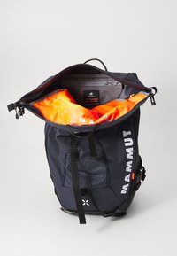 Svart ryggsekk med et strukturert rutemønster, oransje indre fôr, justerbare stropper og en glidelåslomme inni. Har logo-trykk.