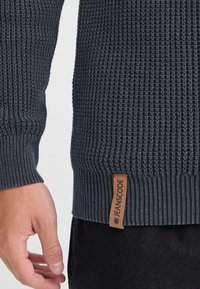 Ciemnoszary sweter wykonany z dzianiny z prążkowanymi mankietami i dolnym wykończeniem. Posiada skórzaną metkę z logo "JEANSCODE". Teksturowana tkanina o dopasowanym kroju.