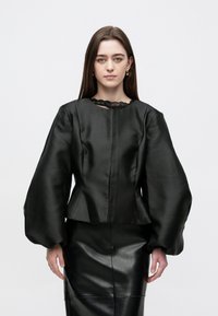 Bluza neagră din satin cu mâneci lungi și voluminoase și decolteu din dantelă. Purta cu o fustă neagră din piele, având un design ajustat.