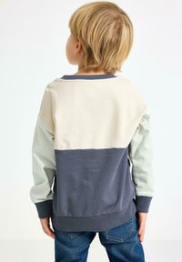 Pullover color-block in tonalità crema, verde chiaro e blu navy. Materiale in cotone con polsini e orlo a coste. Design casual con vestibilità rilassata.