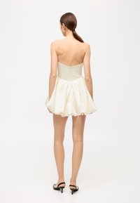 Strapless cream dress with a fitted bodice and a flared skirt, made of smooth fabric. Features a center back zipper and minimal detailing.