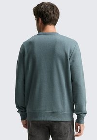  Lichtblauw-groene sweatshirt met een ronde hals en geribbelde boorden. De stof lijkt zacht te zijn met een natuurlijke textuur, en heeft een losvallend ontwerp.