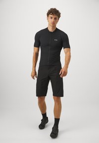 Svart sykkeltrøye med korte ermer og glidelås foran, matchet med svarte shorts. Har en liten logo på brystet og et elegant design.