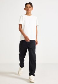 Vit bomull t-shirt med korta ärmar, i kombination med svarta raka byxor och vita sneakers. Enkelt design, inga synliga mönster.