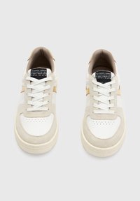 Białe sneakersy z beżowymi zamszowymi akcentami, okrągłym noskiem, płaskimi sznurówkami i perforowanym noskiem. Posiadają metkę z logo na języku i kontrastowy pasek po bokach.
