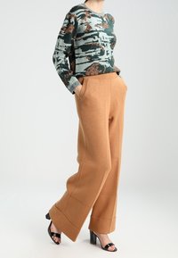 Zielony sweter zrobiony na drutach z brązowym wzorem, zestawiony z brązowymi, szerokimi spodniami z wysokim stanem i czarnymi sandałami na obcasie.