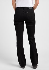 Svarta utsvängda jeans gjorda av denim; har två bakfickor med dekorativ sömnad och ett läderackent vid midjan.