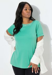 Zelená krátkosrstá košile s kulatým výstřihem zdobená rhinestony. Lehká tkanina a volný střih, doplněná bílou vrstvou pod ní.