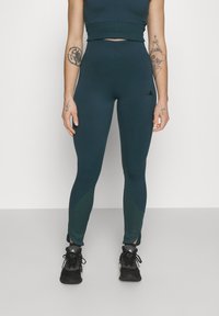 Colanți de sport teal cu un design ajustat, fabricați dintr-un material neted. Au accente texturate la picioare și un mic logo pe șold.