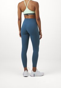 Blue high-waisted leggings and a light green sports bra, featuring a black "Swoosh" logo on the band. White athletic shoes with colorful accents.