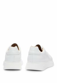 Baskets en cuir blanc avec logo "BOSS" embossé sur les languettes de talon, semelles épaisses en caoutchouc blanc, vues de dos sur fond blanc.